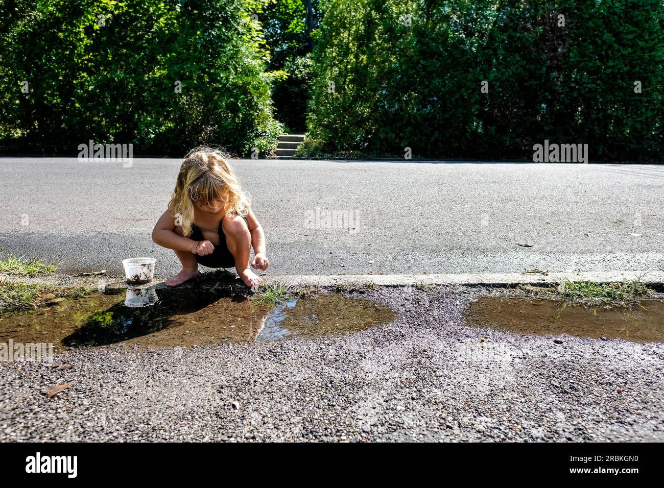fille jouant dehors pieds nus dans des flaques sur le trottoir Banque D'Images