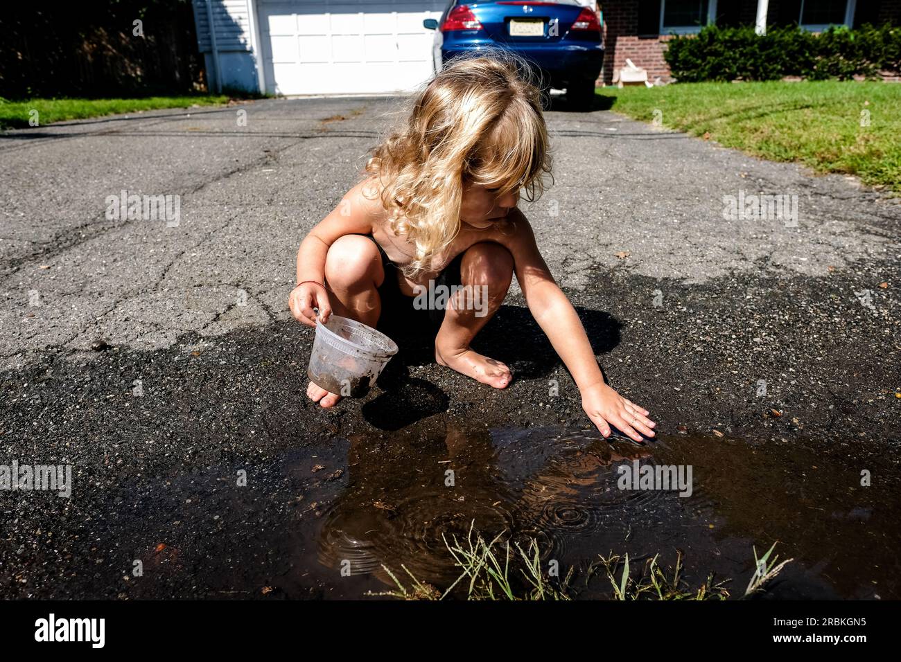 fille jouant dehors dans la flaque d'eau dans l'allée dans la lumière du soleil Banque D'Images