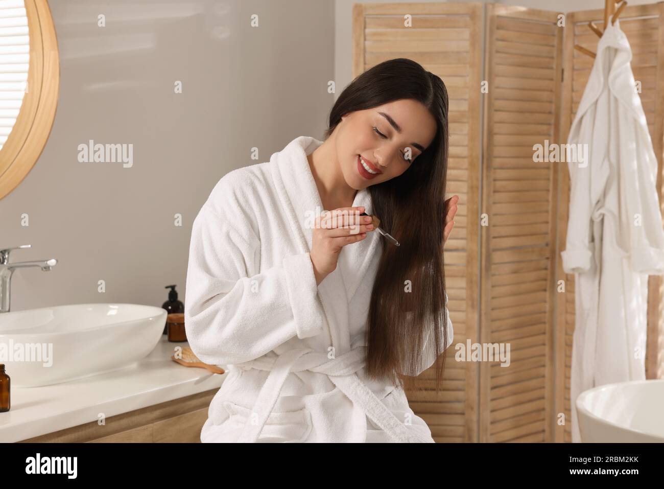 Heureuse jeune femme appliquant de l'huile essentielle sur les cheveux dans  la salle de bain Photo Stock - Alamy
