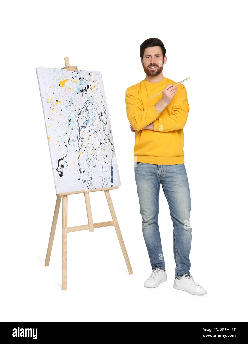 Homme heureux avec brosse près du chevalet avec peinture sur fond blanc. Passe-temps créatif Banque D'Images
