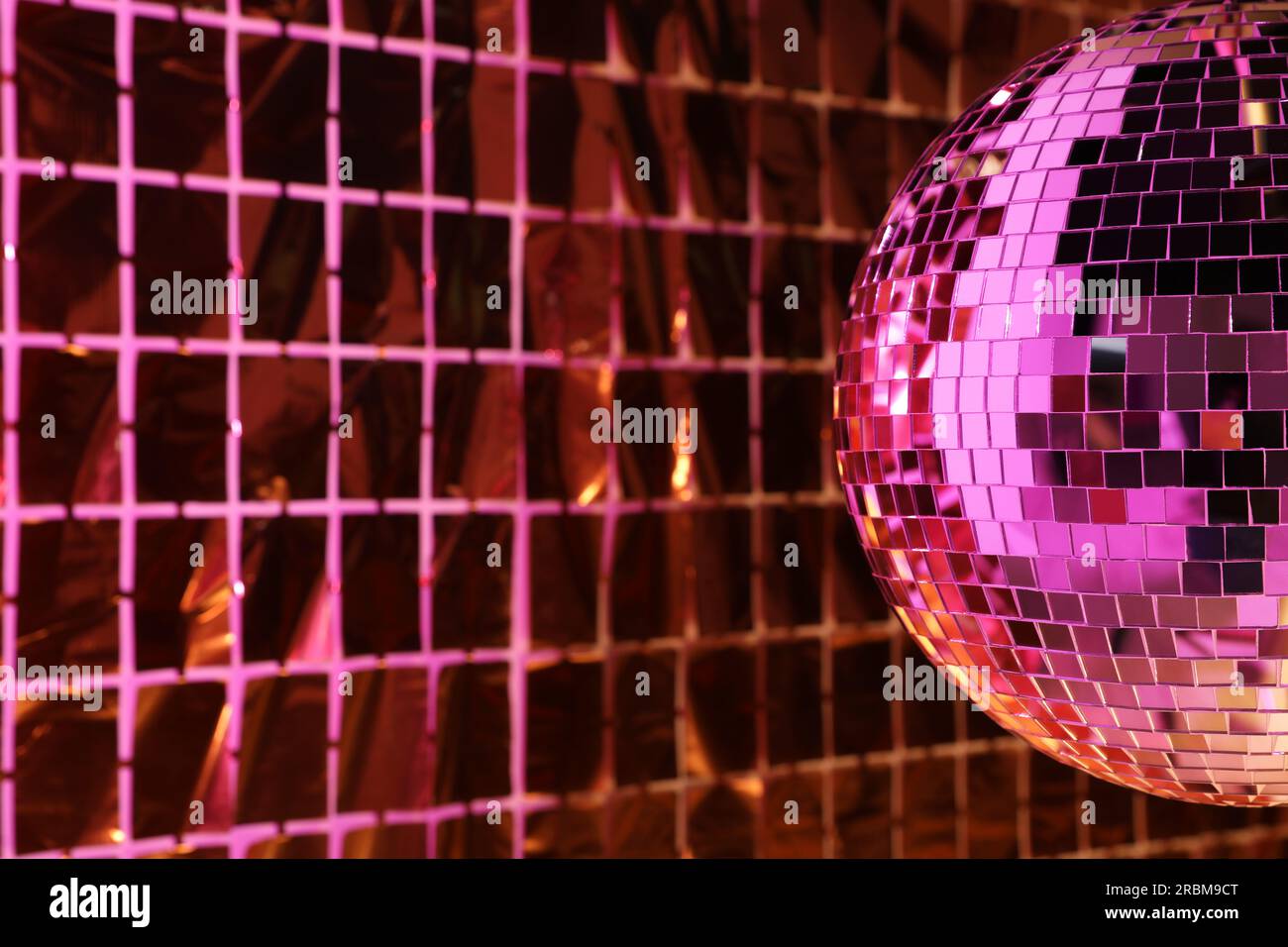 Boule disco brillante contre le rideau de fête de papier aluminium sous la lumière rose, espace pour le texte Banque D'Images