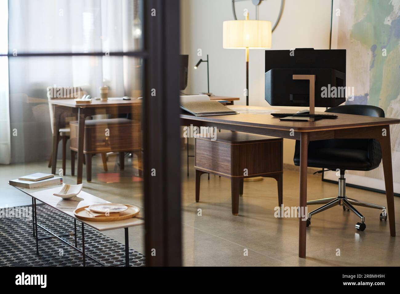 Partie de l'espace de coworking avec bureaux en bois, écran d'ordinateur, lampe, fauteuil, longue petite table pour déjeuner et armoire en bois Banque D'Images