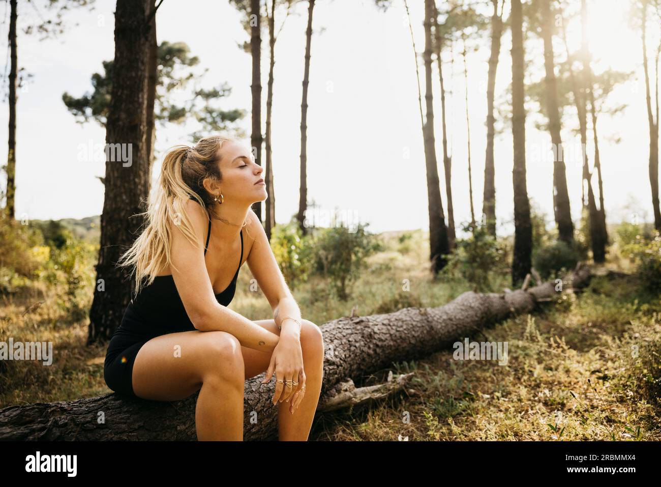 Jeune coureuse féminine s'arrêtant pour un repos sur un tronc d'arbre. Femme de fitness prenant une pause de l'entraînement en plein air dans une forêt. Banque D'Images
