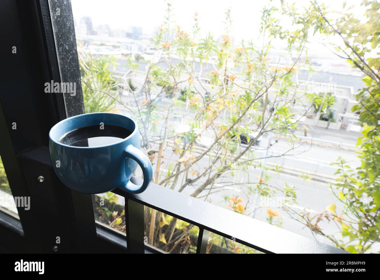Tasse à café équilibrée sur une balustrade de balcon, avec cimes d'arbre au-delà. Maison, détente et vie domestique. Banque D'Images