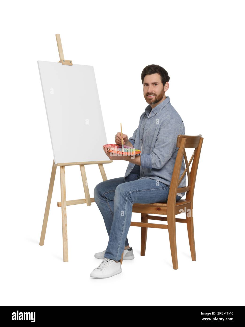 Homme heureux avec pinceau et palette près du chevalet avec toile. Passe-temps créatif Banque D'Images