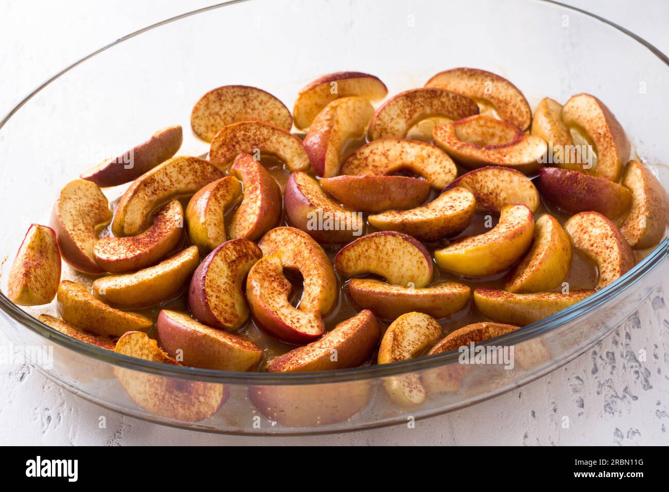 Tranches de pommes cuites au four avec cannelle, miel et citron dans un plat allant au four en verre sur fond bleu clair. Délicieux dessert végétalien maison, cuisine Banque D'Images