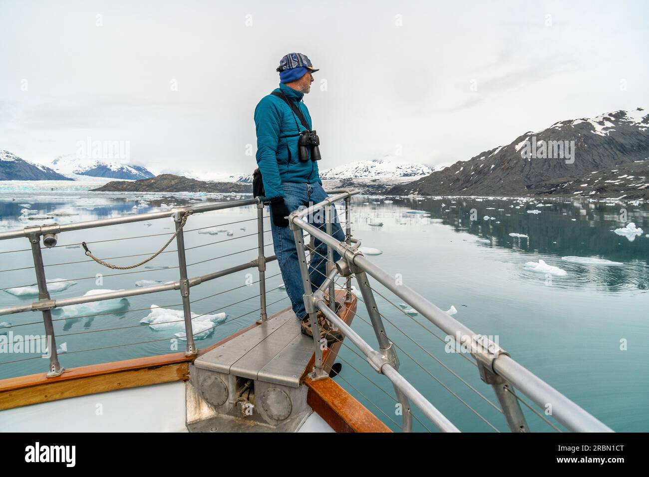 Homme caucasien mûr debout sur la plate-forme de proue d'un bateau regardant une scène avec iceberg dans l'eau, Columbia Glacier ; Prince William Sound, Alask Banque D'Images