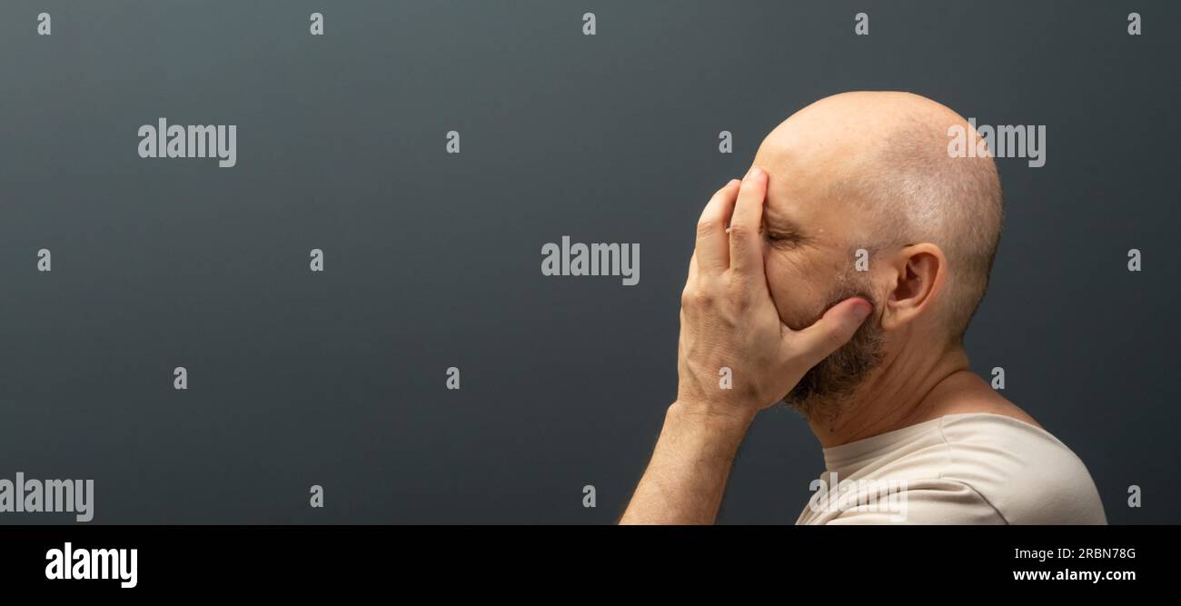 Triste homme souffrant de maux de tête ou de migraine. Un gars stressé avec une expression faciale douloureuse qui ressent une faiblesse ou une dépression terrible. Isolé sur bac foncé Banque D'Images