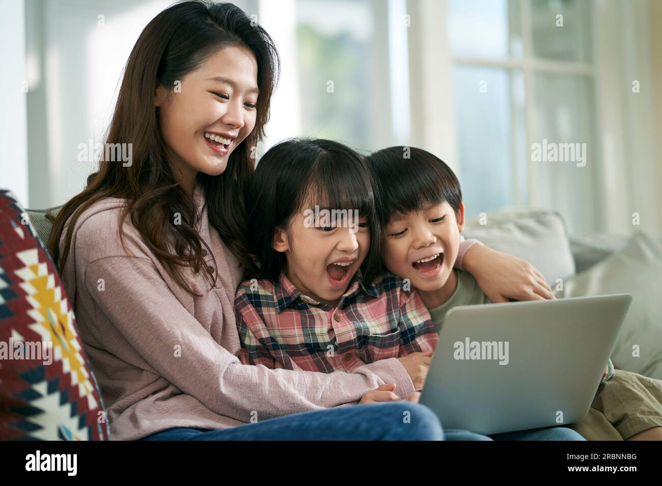 une jeune mère asiatique et deux enfants assis sur un canapé de famille à la maison en utilisant un ordinateur portable ensemble Banque D'Images