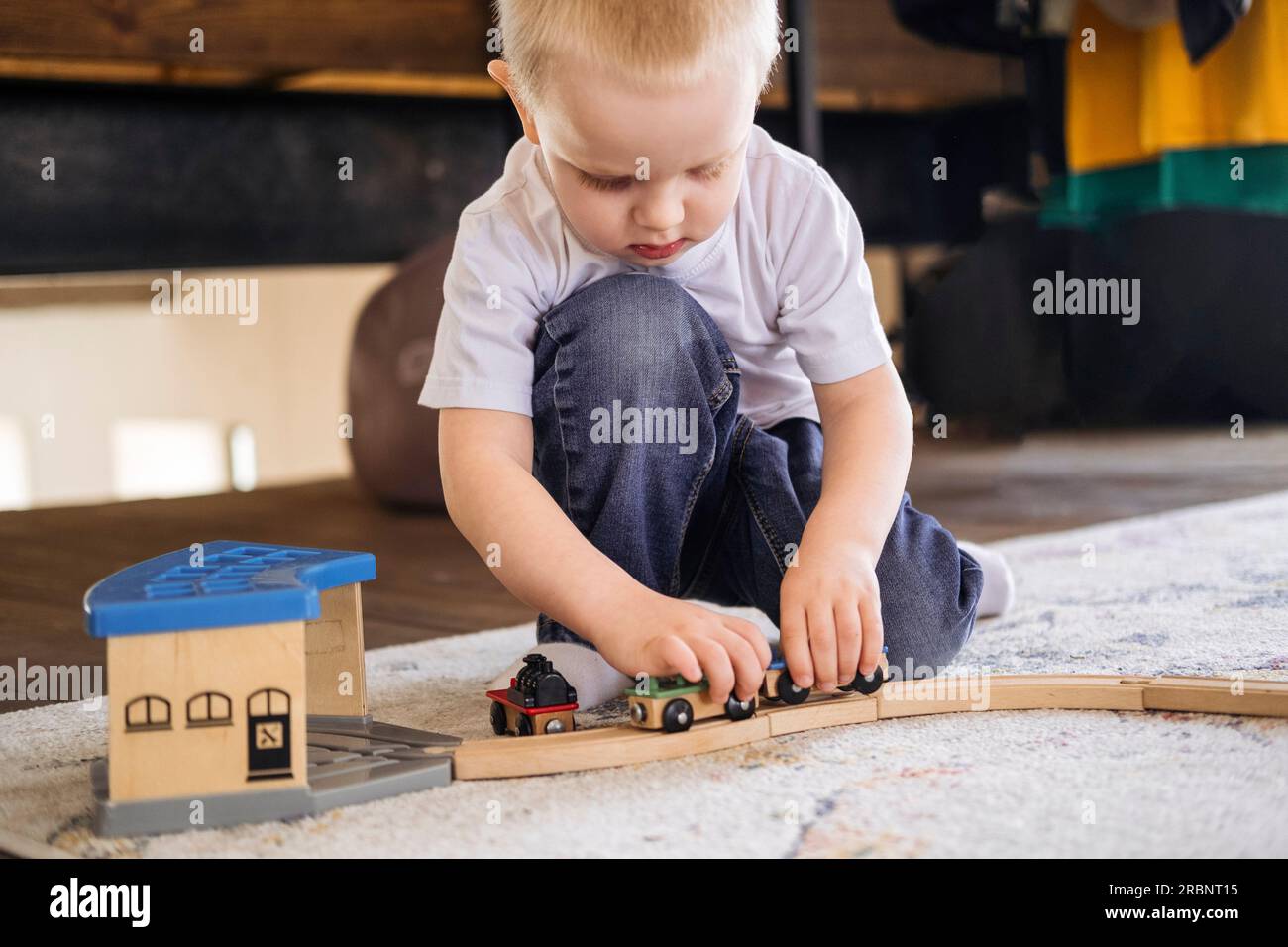 Le petit est assis sur le sol et joue avec le chemin de fer des enfants. Le gamin passe du temps à jouer Banque D'Images