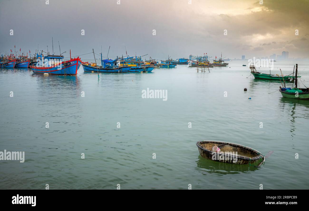 Un coracle abandonné et des bateaux de pêche en bois amarrés sous la pluie à Thọ Quang, Sơn Trà, Danang, Vietnam Banque D'Images