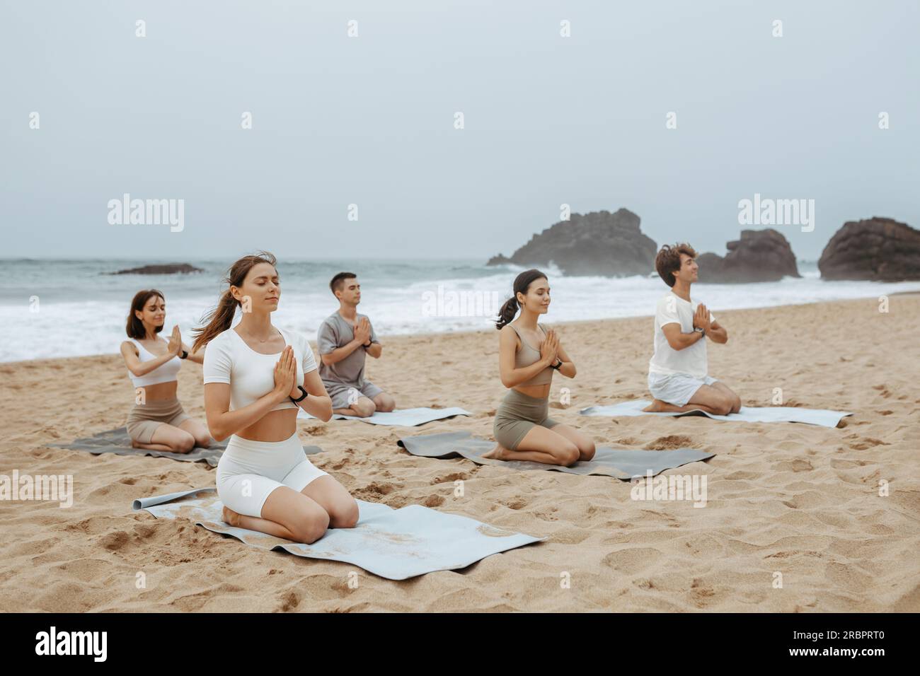 Les gens assis et méditant sur la plage, pratiquant l'asana avec les mains jointes, profitant de l'entraînement matinal sur la côte Banque D'Images