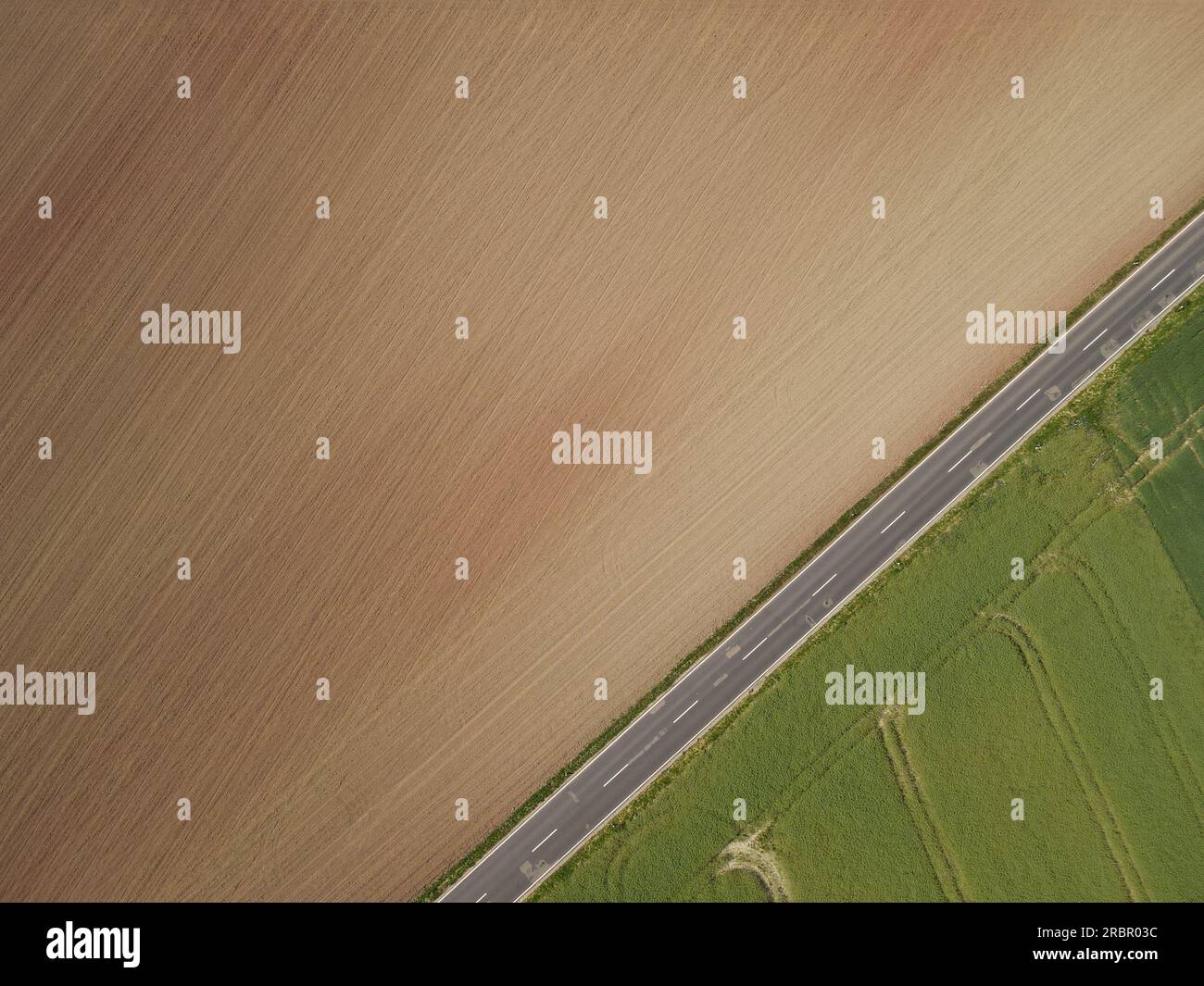Vue de dessus des champs agricoles avec récolte verte, sol labouré brun et une route asphaltée en été Banque D'Images