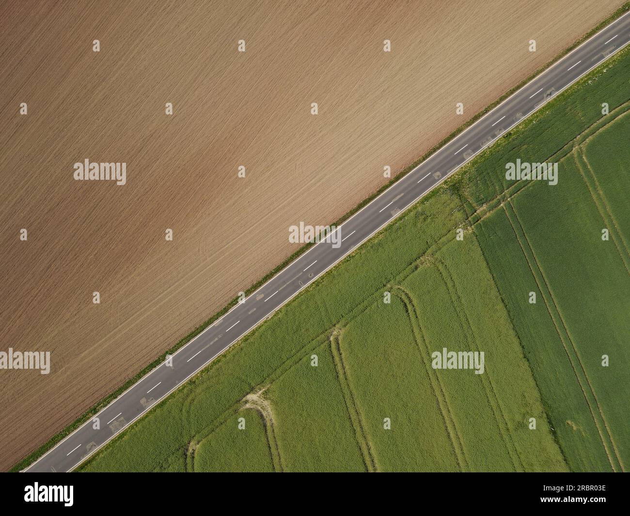 Vue aérienne d'une route asphaltée dans le paysage entre le champ agricole labouré brun avec le sol et un champ vert de croissance avec la culture Banque D'Images