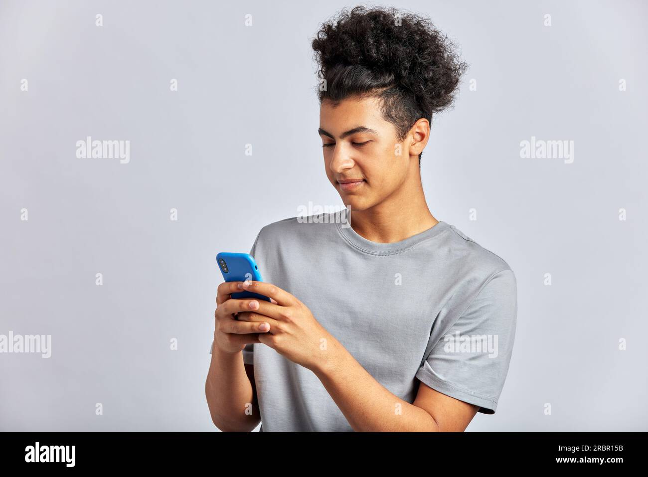 Portrait en studio d'un jeune bel homme brunette aux cheveux bouclés tenant un smartphone dans ses mains. Un mec tordu tapant un message sur un téléphone portable. Mo Banque D'Images