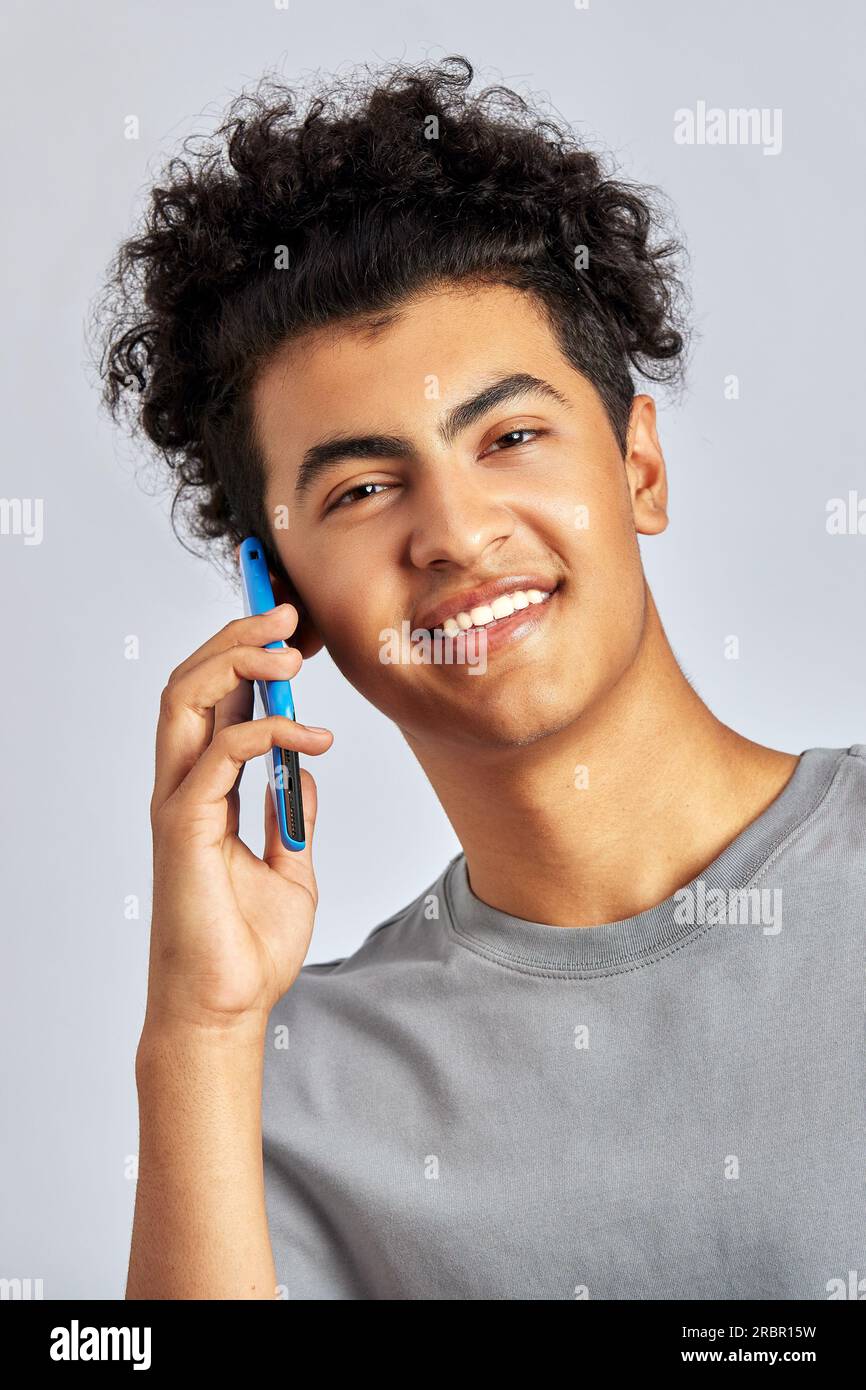 Portrait en studio d'un jeune bel homme brunette aux cheveux bouclés tenant un smartphone dans sa main. Un mec tordu sourit et parle sur un téléphone portable. M Banque D'Images