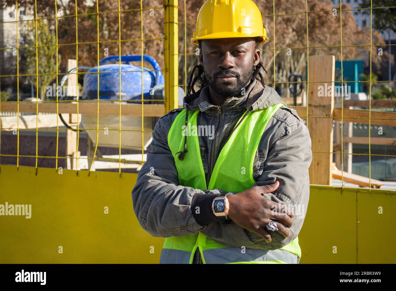 Portrait d'un jeune homme ingénieur africain portant un casque jaune, une veste et un gilet, heureux debout avec les bras croisés regardant la caméra, concep d'ingénierie Banque D'Images