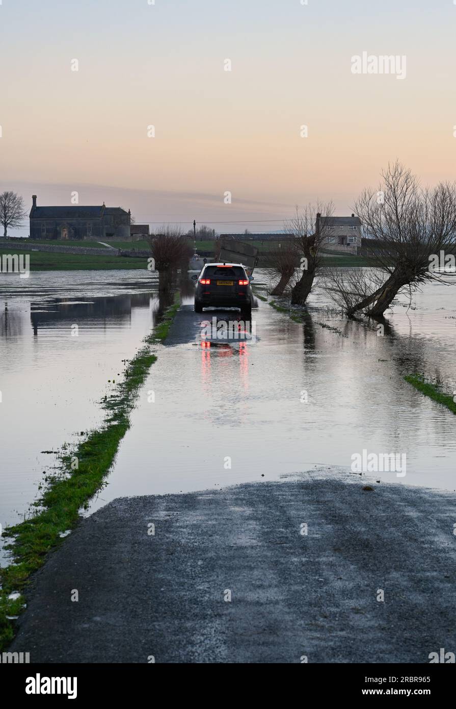 Voiture conduisant à travers la route inondée Godney près de Glastonbury sur les niveaux Somerset Banque D'Images