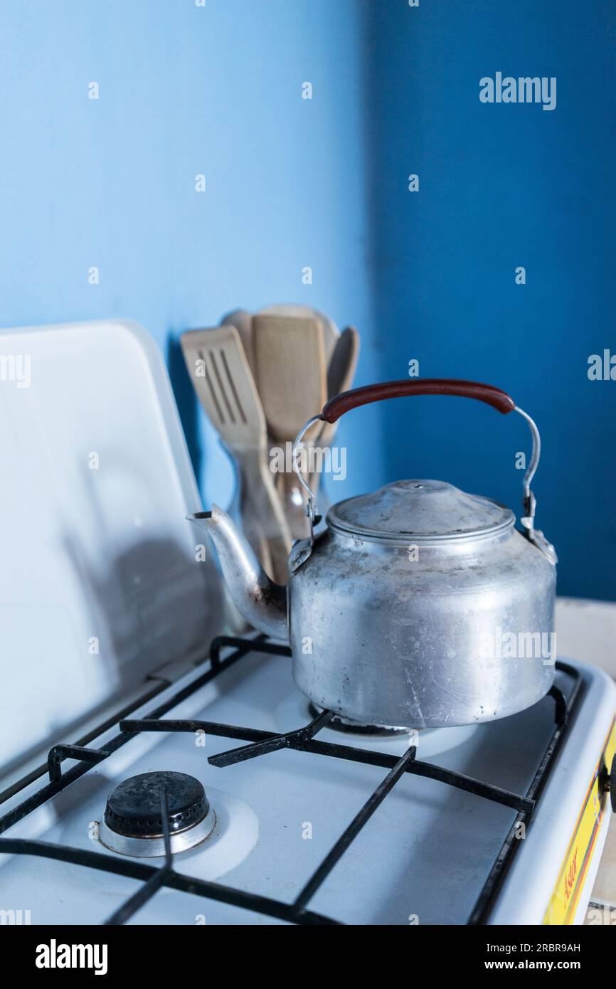 bouilloire à thé en aluminium rayé sur la table de cuisson à gaz devant les murs bleus et avec un pot d'outils de cuisine en bois et bambou dans un vase en verre, Jinotega, ni Banque D'Images