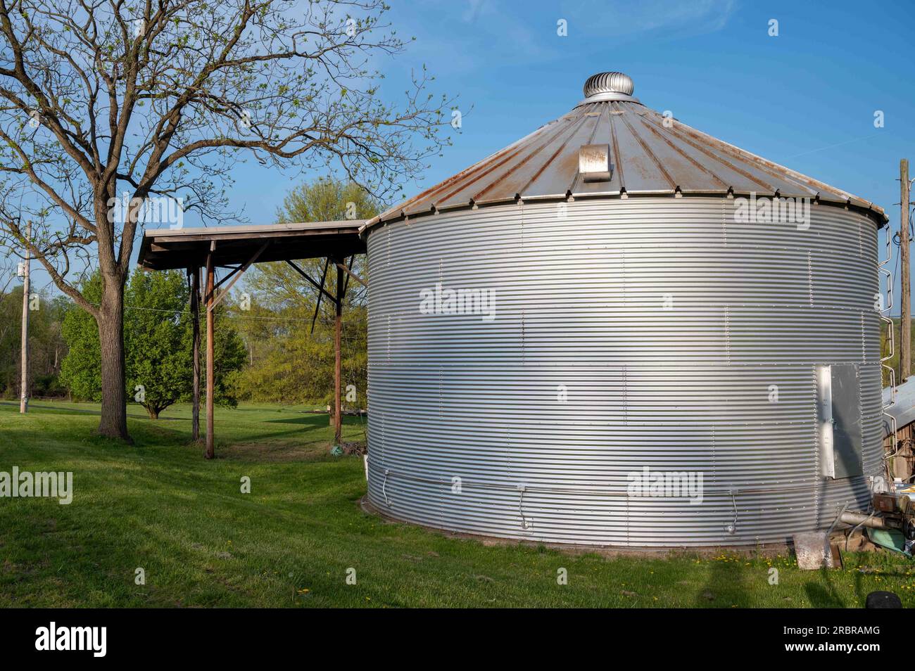 Stockage et séchoir d'alimentation en soja à grain ondulé en acier inoxydable excentré sous un ciel bleu sur un champ agricole herbeux. Pas de personnes, avec espace de copie. Acric Banque D'Images