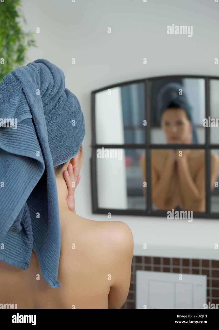 Femme dans la salle de bain avec une serviette sur la tête regarde dans le miroir Banque D'Images