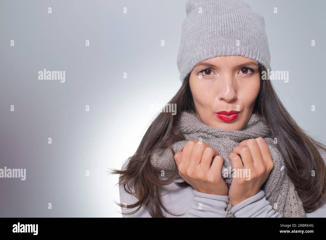 Jolie jeune femme à la mode hivernale câlinant à l'intérieur de son jersey tricoté en laine gris, écharpe et casquette sur une journée froide avec Copyspace Banque D'Images