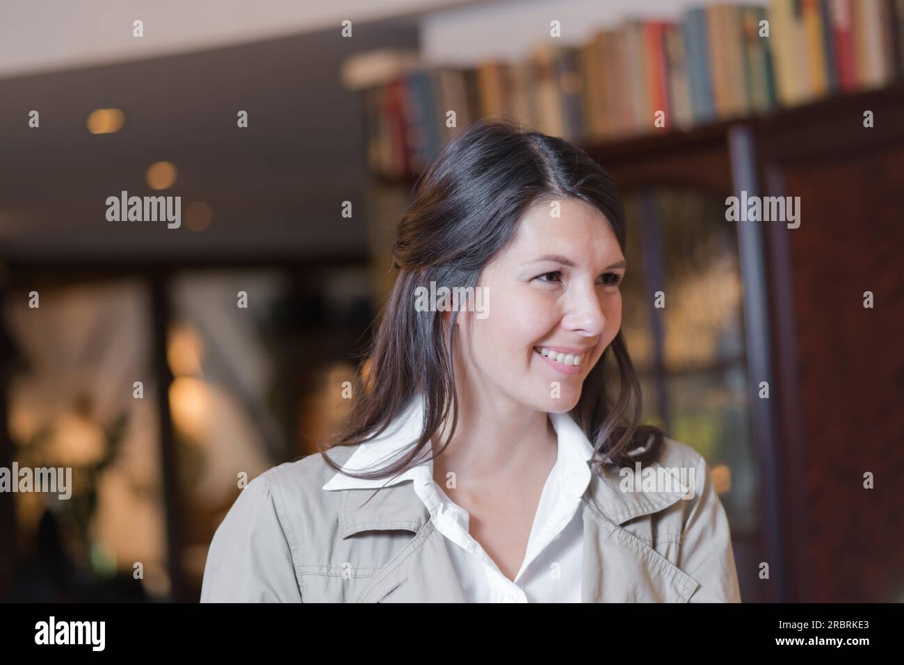 Smiling attractive young female guest dans un hall de l'hôtel parlant à la réceptionniste qu'elle vérifie à son arrivée en Banque D'Images