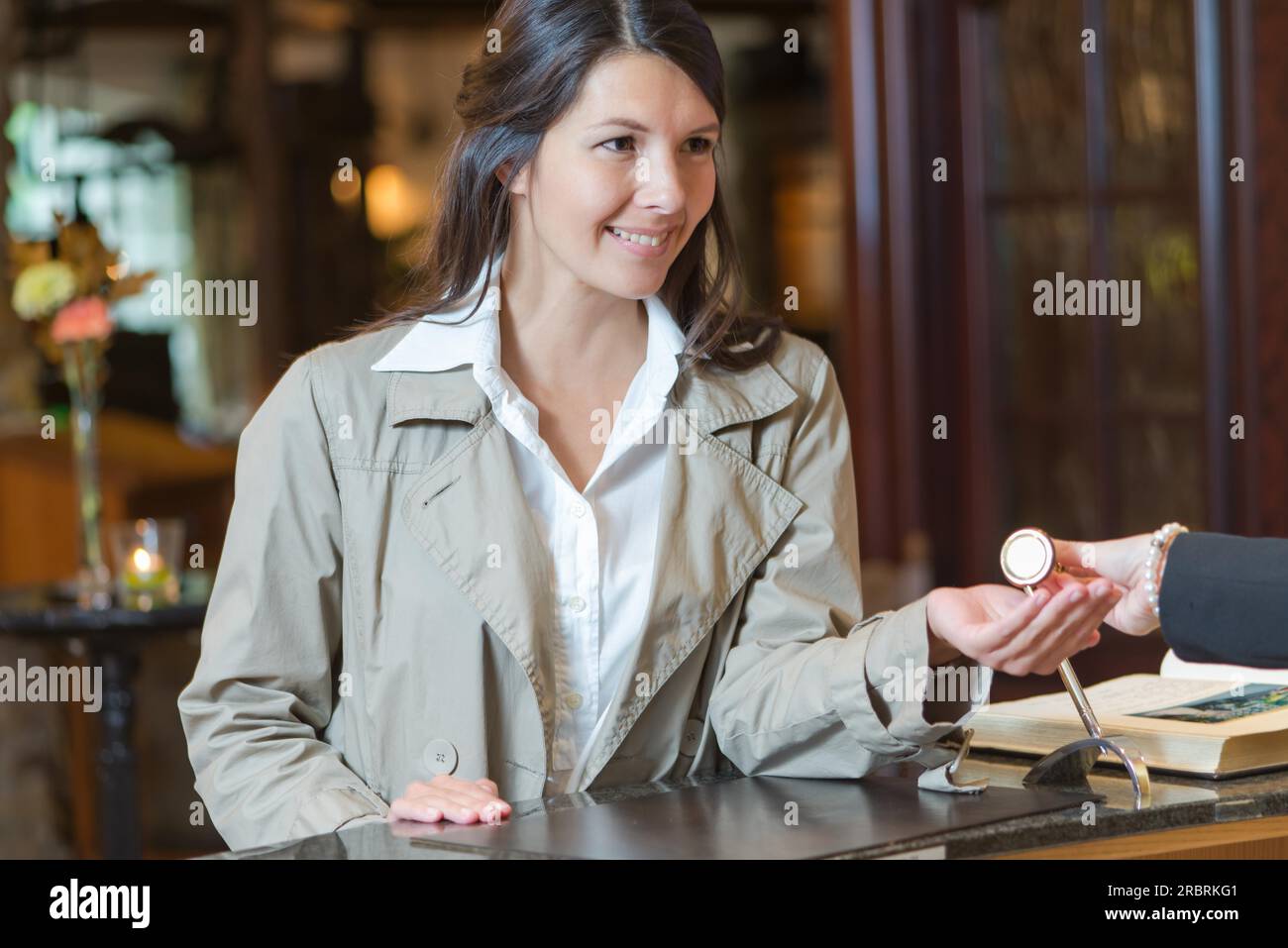 Smiling attractive young female guest dans un hall de l'hôtel parlant à la réceptionniste qu'elle vérifie à son arrivée en Banque D'Images
