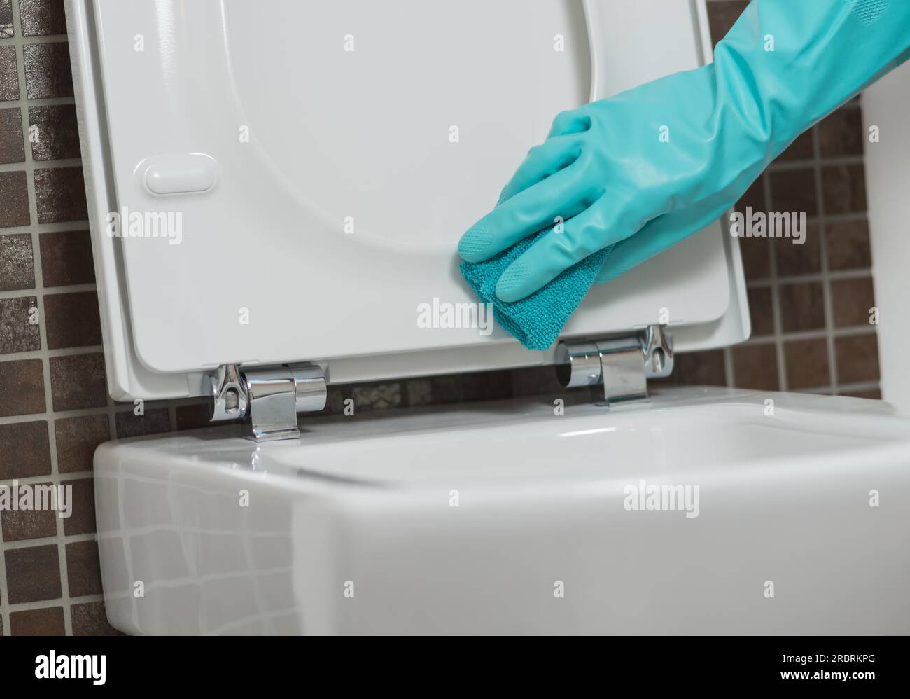 Main d'une personne nettoyant le siège de toilette dans des gants en caoutchouc avec une éponge désinfectant le dessous pour les germes et les bactéries tout en effectuant le ménage Banque D'Images