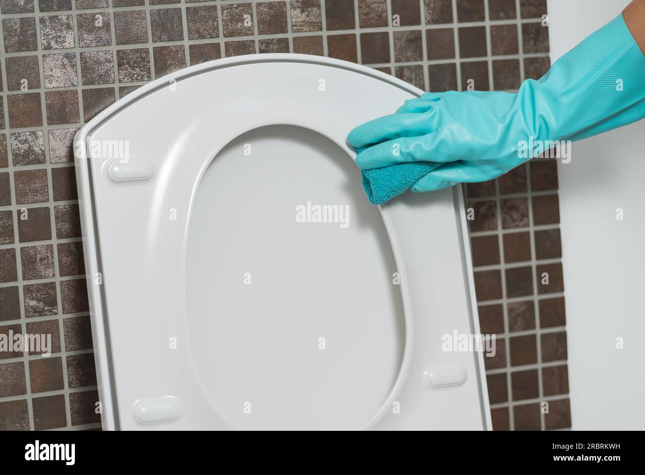Main d'une personne nettoyant le siège de toilette dans des gants en caoutchouc avec une éponge désinfectant le dessous pour les germes et les bactéries tout en effectuant le ménage Banque D'Images