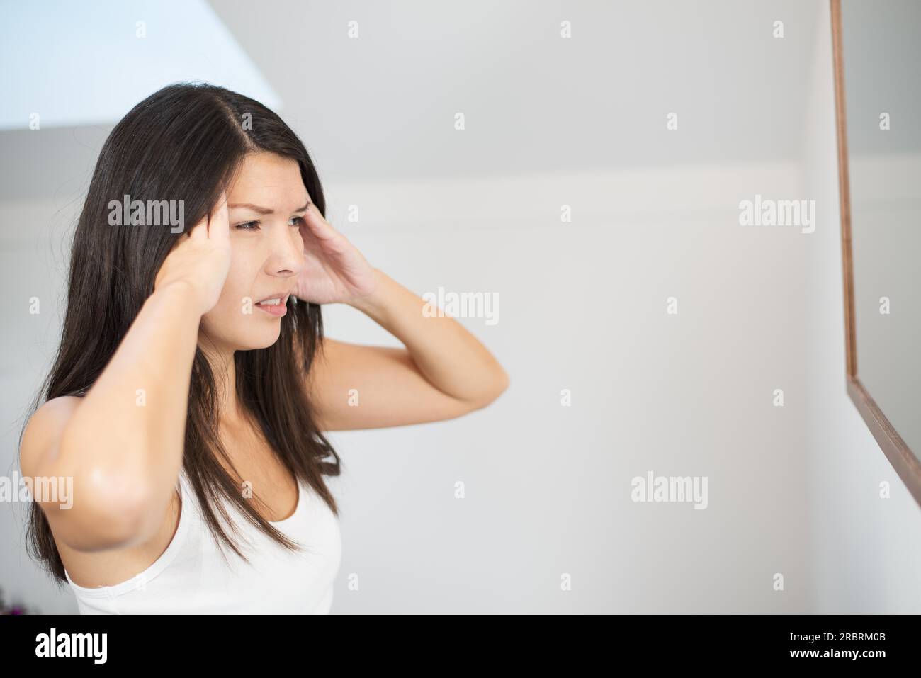 Jolie jeune femme avec un mal de tête migraineux debout tenant ses doigts à ses tempes avec ses yeux à moitié fermés dans la douleur Banque D'Images