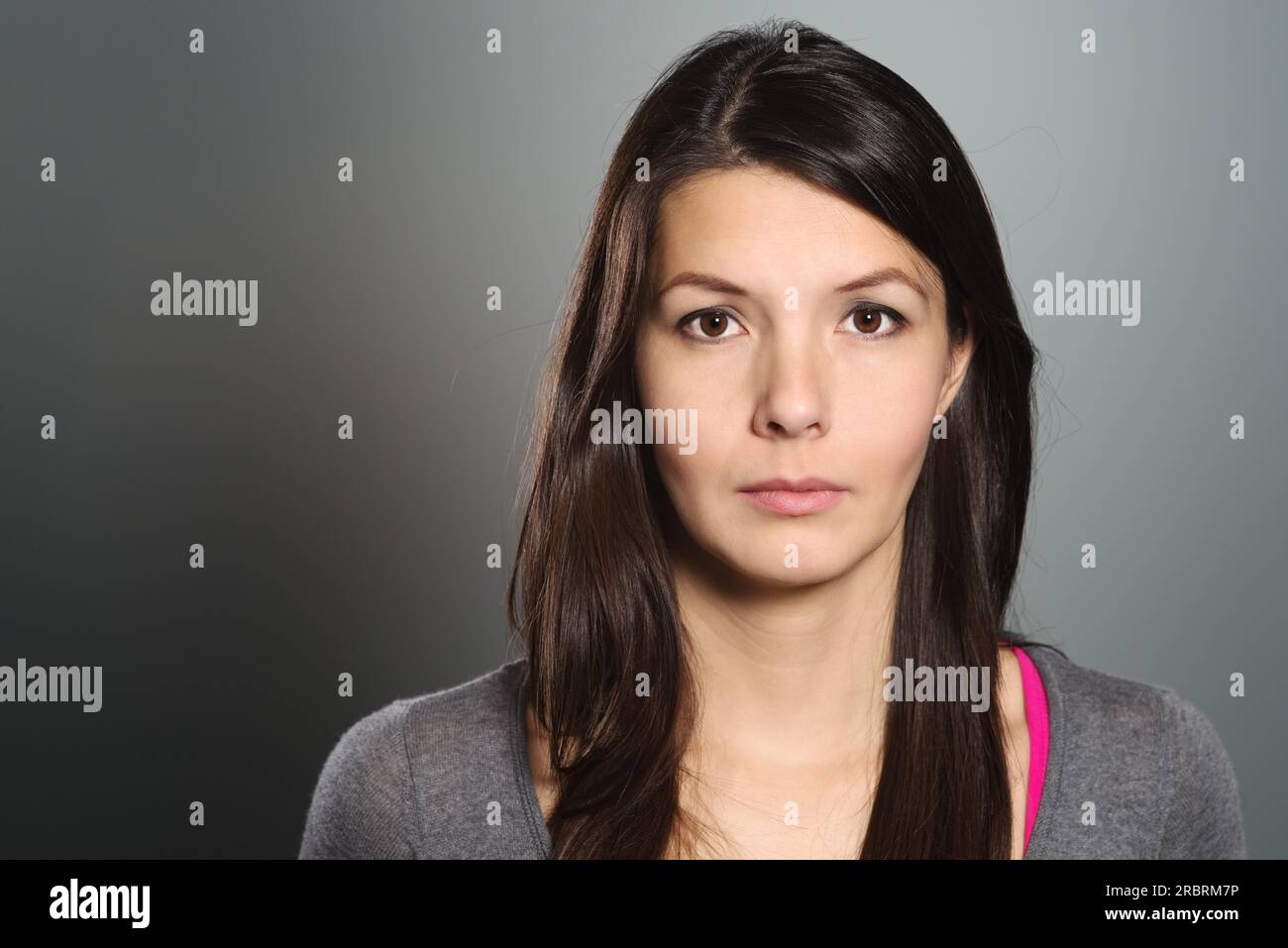 Studio tête et épaules portrait sur gris d'une belle jeune femme sérieuse regardant directement la caméra Banque D'Images