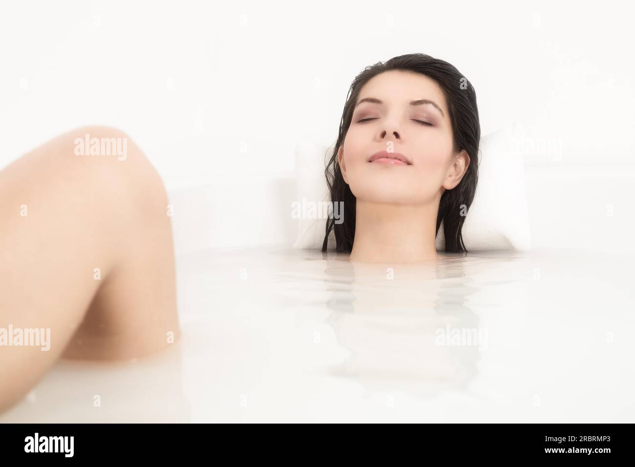 Blissful belle jeune femme se faisant dorloter dans un bain chaud avec juste son visage visible au-dessus de l'eau savonneuse alors qu'elle se détend avec une sérénité Banque D'Images