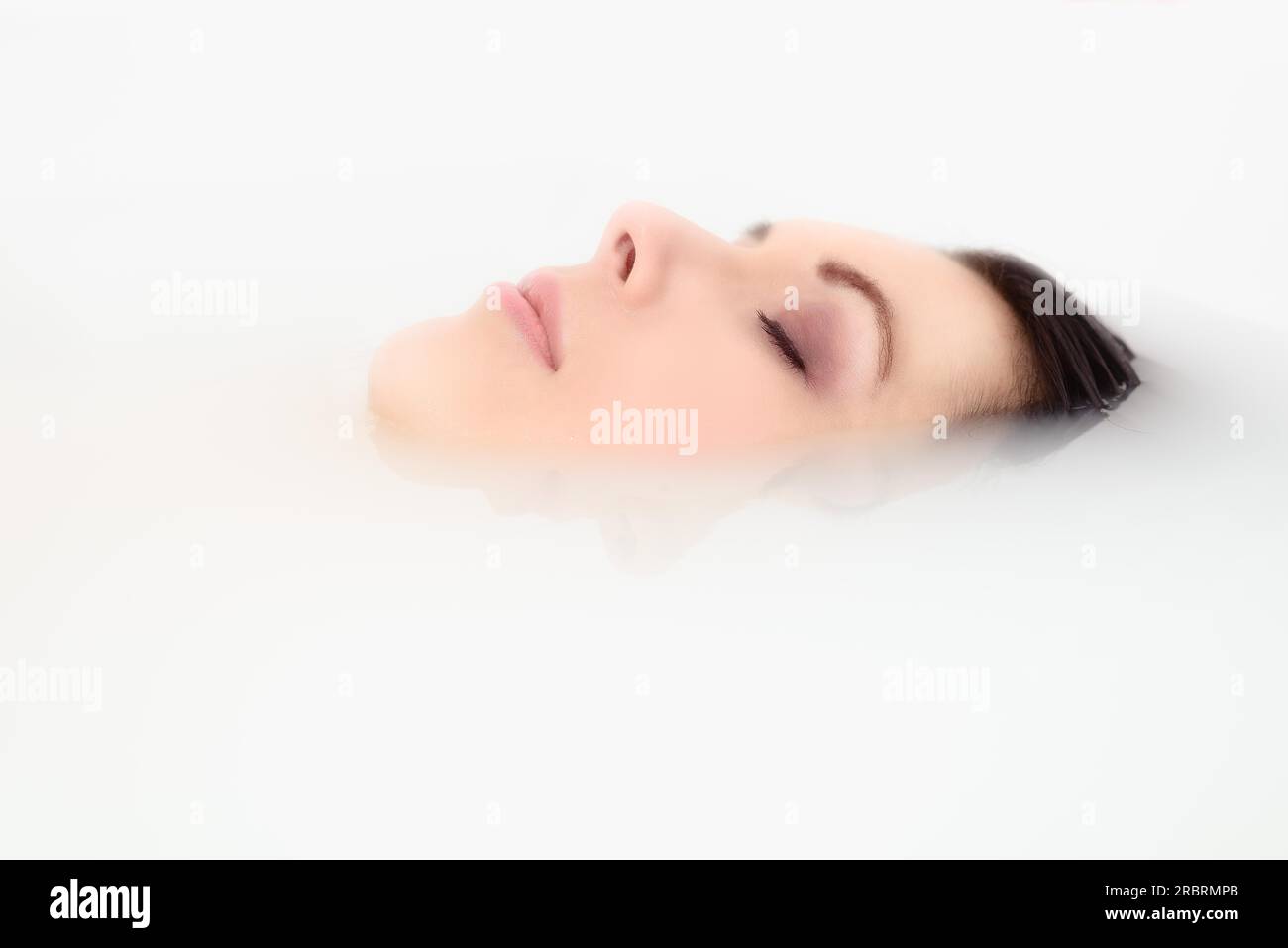 Blissful belle jeune femme se faisant dorloter dans un bain chaud avec juste son visage visible au-dessus de l'eau savonneuse alors qu'elle se détend avec une sérénité Banque D'Images