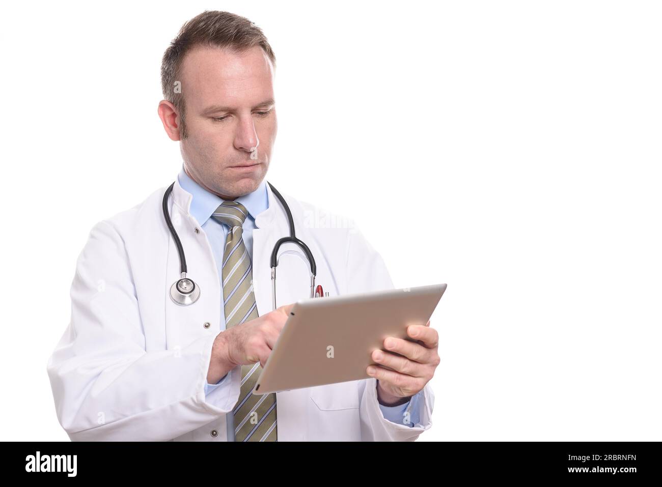 Médecin professionnel masculin dans un manteau blanc debout consultant un ordinateur tablette lisant l'information avec une expression sérieuse, isolé sur blanc Banque D'Images