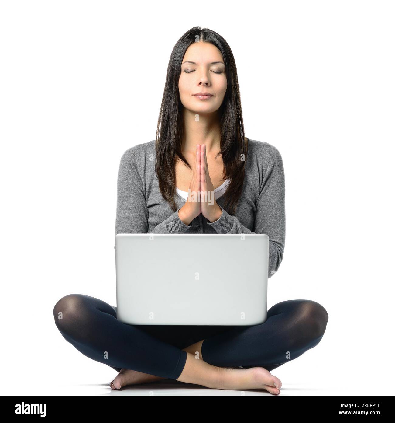 Jolie femme aux cheveux longs en posture méditante avec les yeux fermés et les jambes croisées tout en faisant face à un ordinateur portable en face. Isolé sur fond blanc Banque D'Images