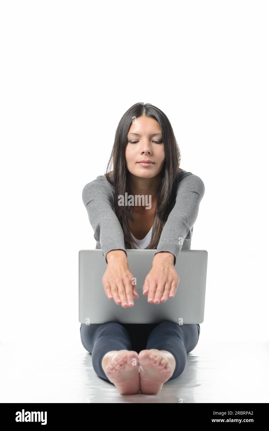 Séduisante jeune femme assise pieds nus sur le sol avec son ordinateur portable étirant ses mains et les pieds se relaxant tout en méditant avec fermé Banque D'Images