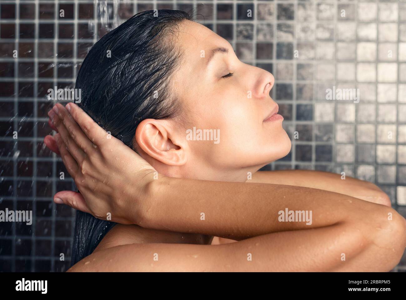 Belle femme lavant ses cheveux dans la douche rinçant sous le jet d'eau avec sa tête inclinée vers l'arrière et les yeux fermés dans un soin des cheveux Banque D'Images