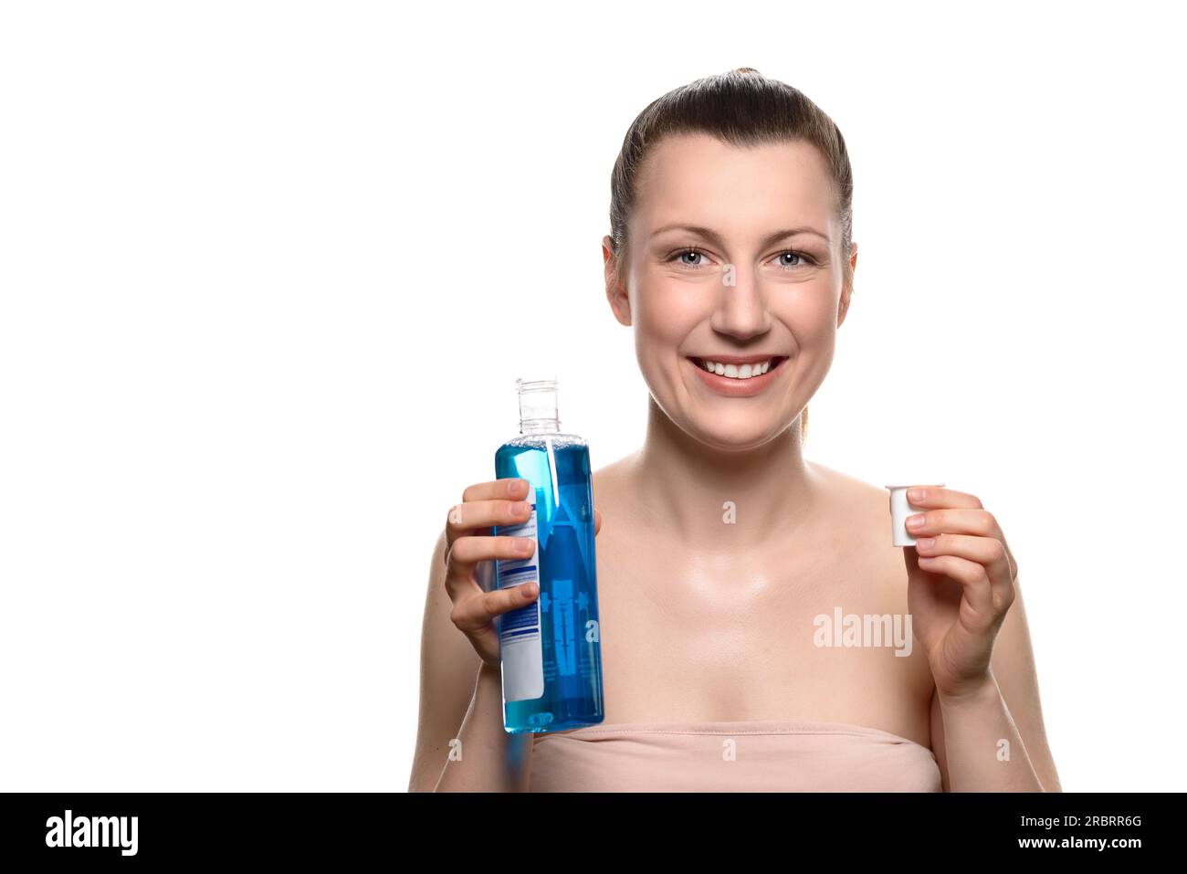 Gros plan sourire Jeune femme tenant une bouteille de bain de bouche dans un bouchon tout en regardant la caméra, isolé sur fond blanc Banque D'Images