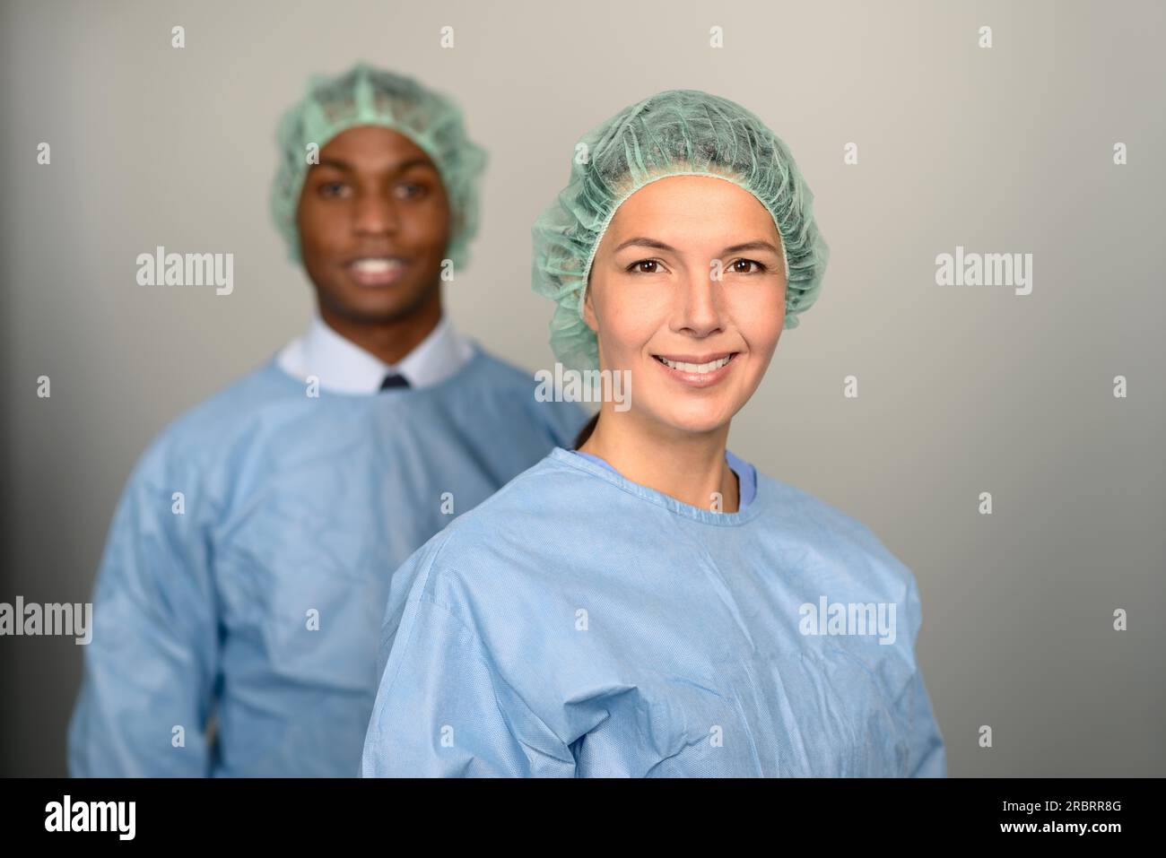 Professionnels de la santé hommes et femmes confiants souriant à l'appareil photo portant des gommages bleus et un capuchon de stérilité Banque D'Images