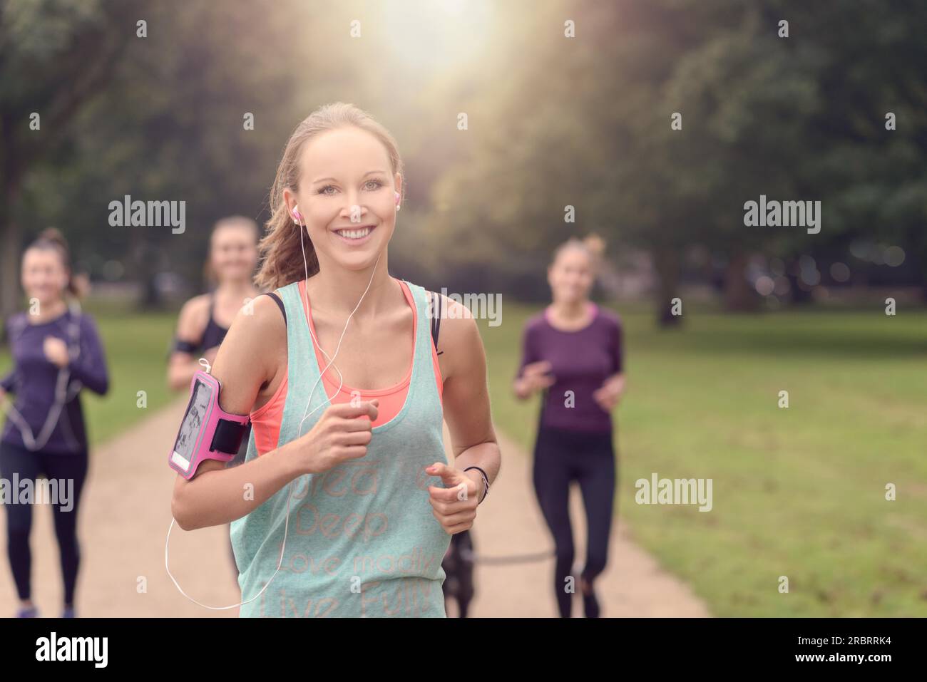 Half Body Shot of a Athletic Pretty Young Woman souriant à la caméra tout en faisant du jogging au parc avec d'autres filles, avec un espace de copie sur la droite Banque D'Images