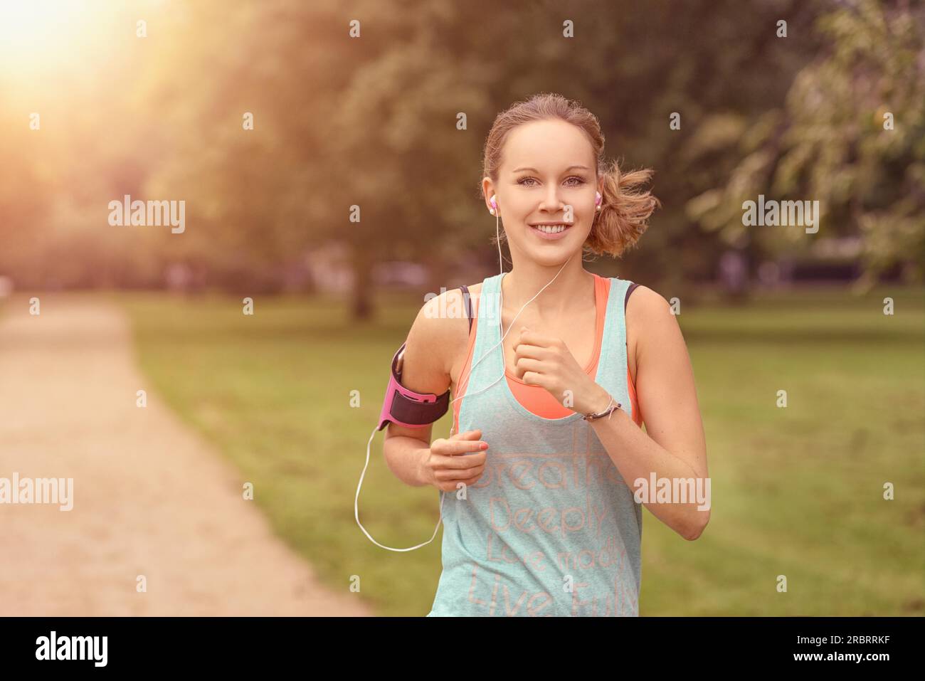 Moitié du corps, tourné d'une jolie femme athlétique jogging au parc avec des écouteurs et souriant à la caméra, avec copie espace Banque D'Images