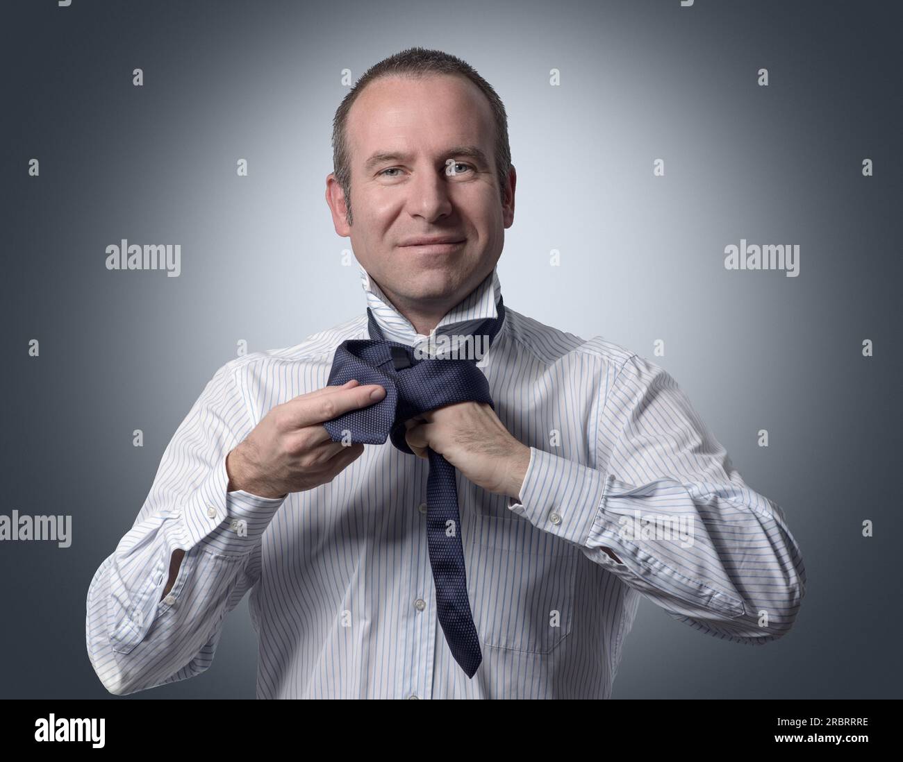 Half Body Shot d'un homme d'affaires adulte Tiant une cravate de cou tout en souriant à la caméra sur fond gris Banque D'Images