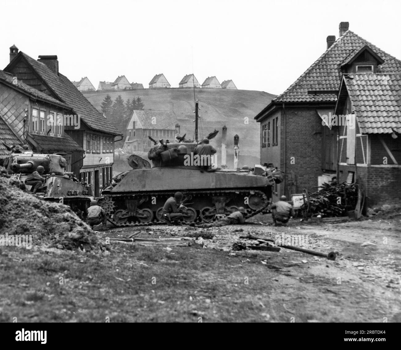 Sankt Andreasberg, Allemagne, le 14 avril 1945 Un char américain balançait de l'autre côté de la rue et offrait une couverture aux fantassins de la 1e division d'infanterie Première armée, alors qu'ils cherchent des tireurs d'élite dans les bâtiments. Banque D'Images