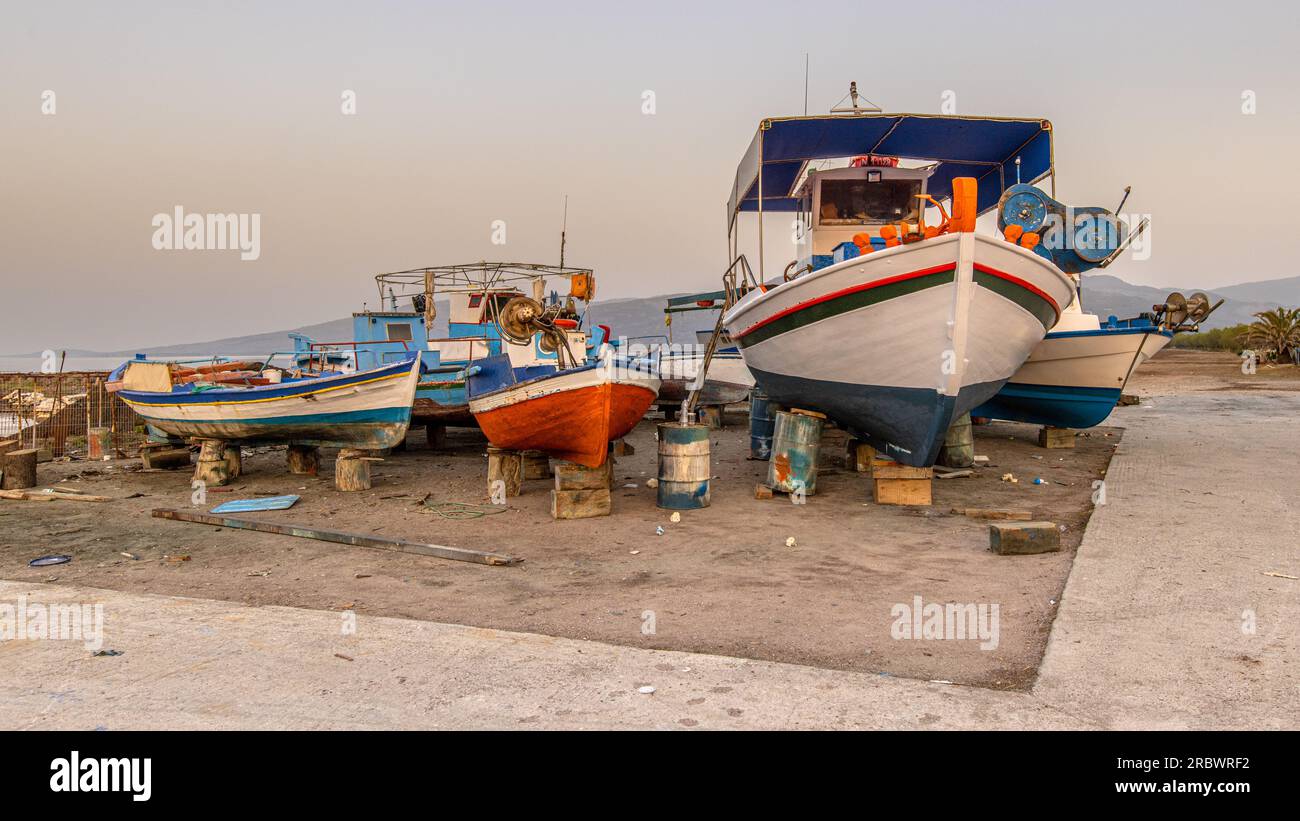 Scène de port de pêche en Grèce avec des bateaux, des palmiers et des scooters au lever du soleil sur une belle journée d'été tranquille Banque D'Images