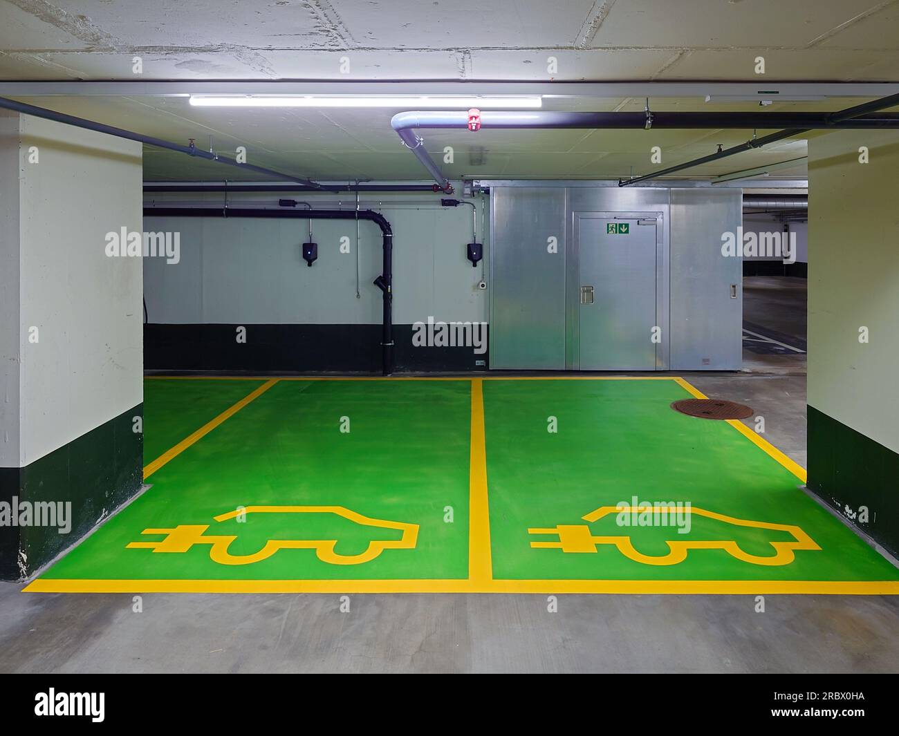 Places de parking souterraines réservées aux véhicules électriques uniquement. Petites prises de charge murales, sol en ciment peint vert, pas de gens. Banque D'Images