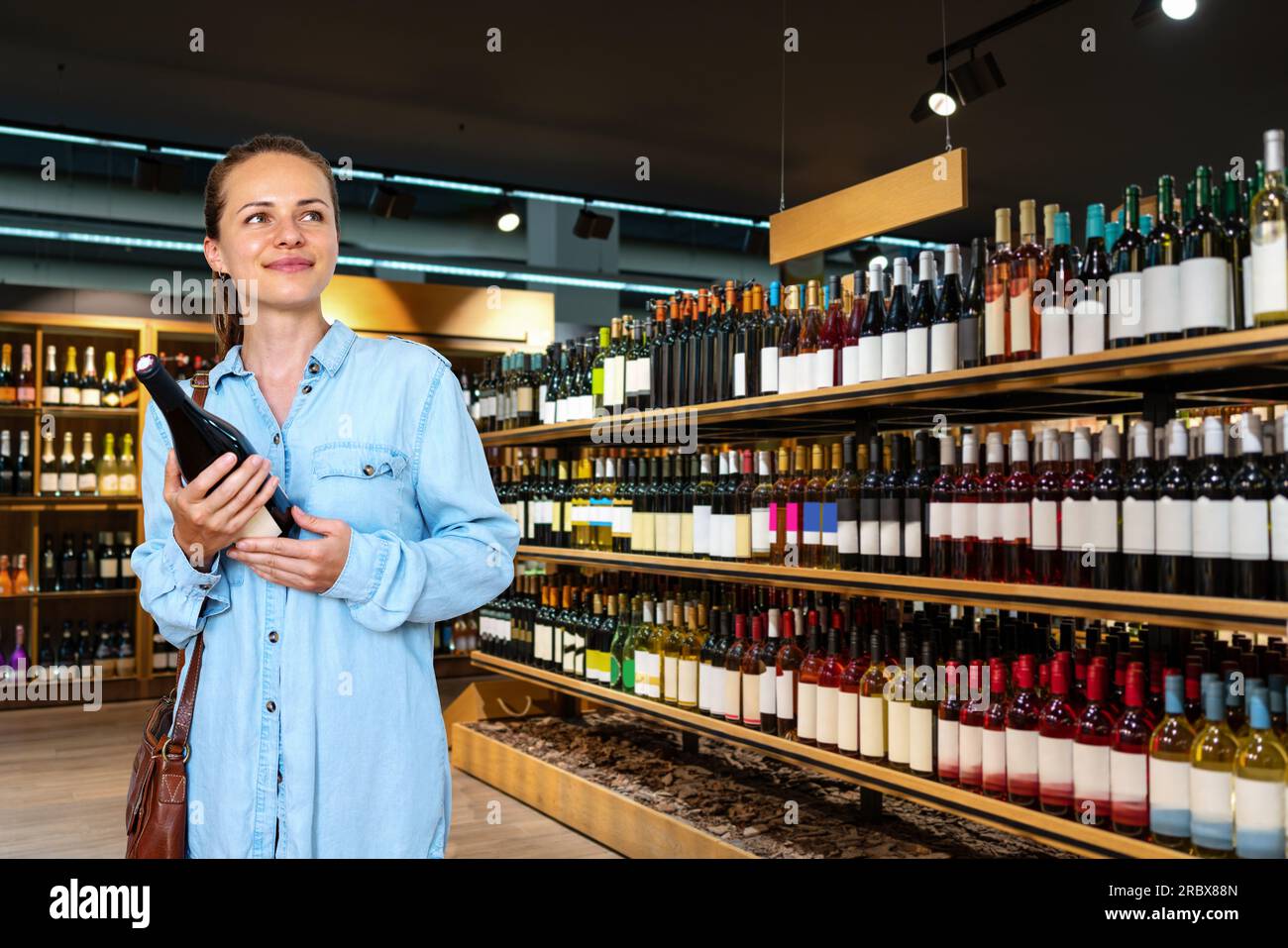 Jeune femme brune adulte choisissant le vin dans le magasin de vin et souriant. Banque D'Images