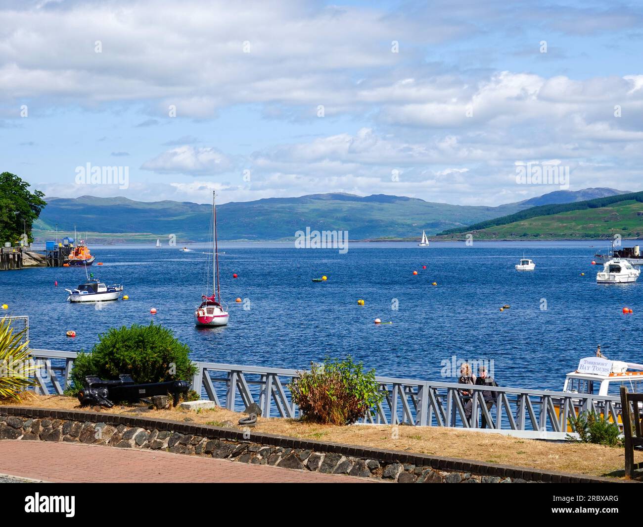 Couple marchant jusqu'à la rampe de la marina à Tobermory Bay sur une belle journée d'été, île de Mull, Écosse, Royaume-Uni. Banque D'Images