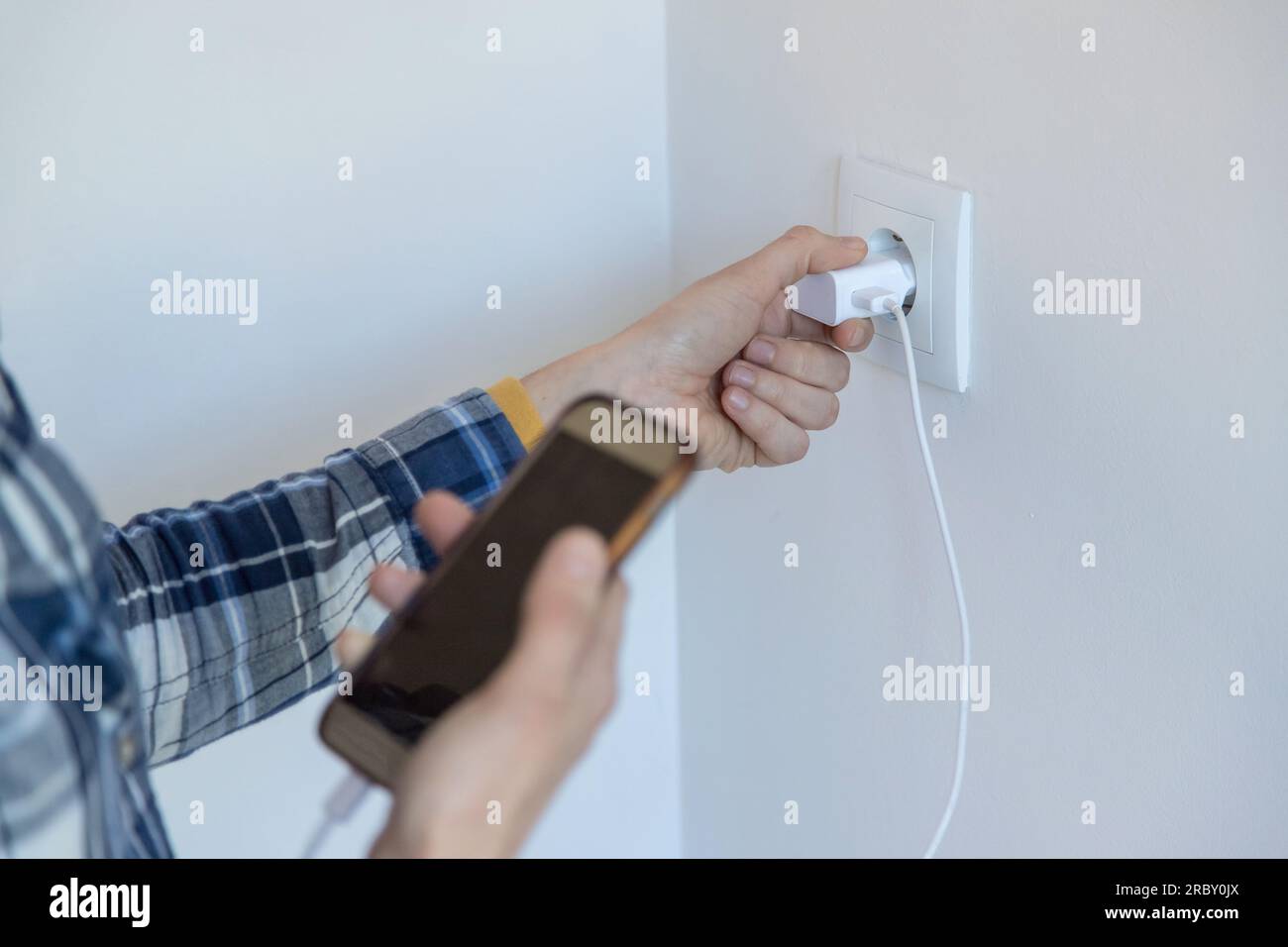 Gros plan d'une personne tenant un smartphone et un chargeur pour le mettre en charge. Image horizontale et espace de copie. Banque D'Images