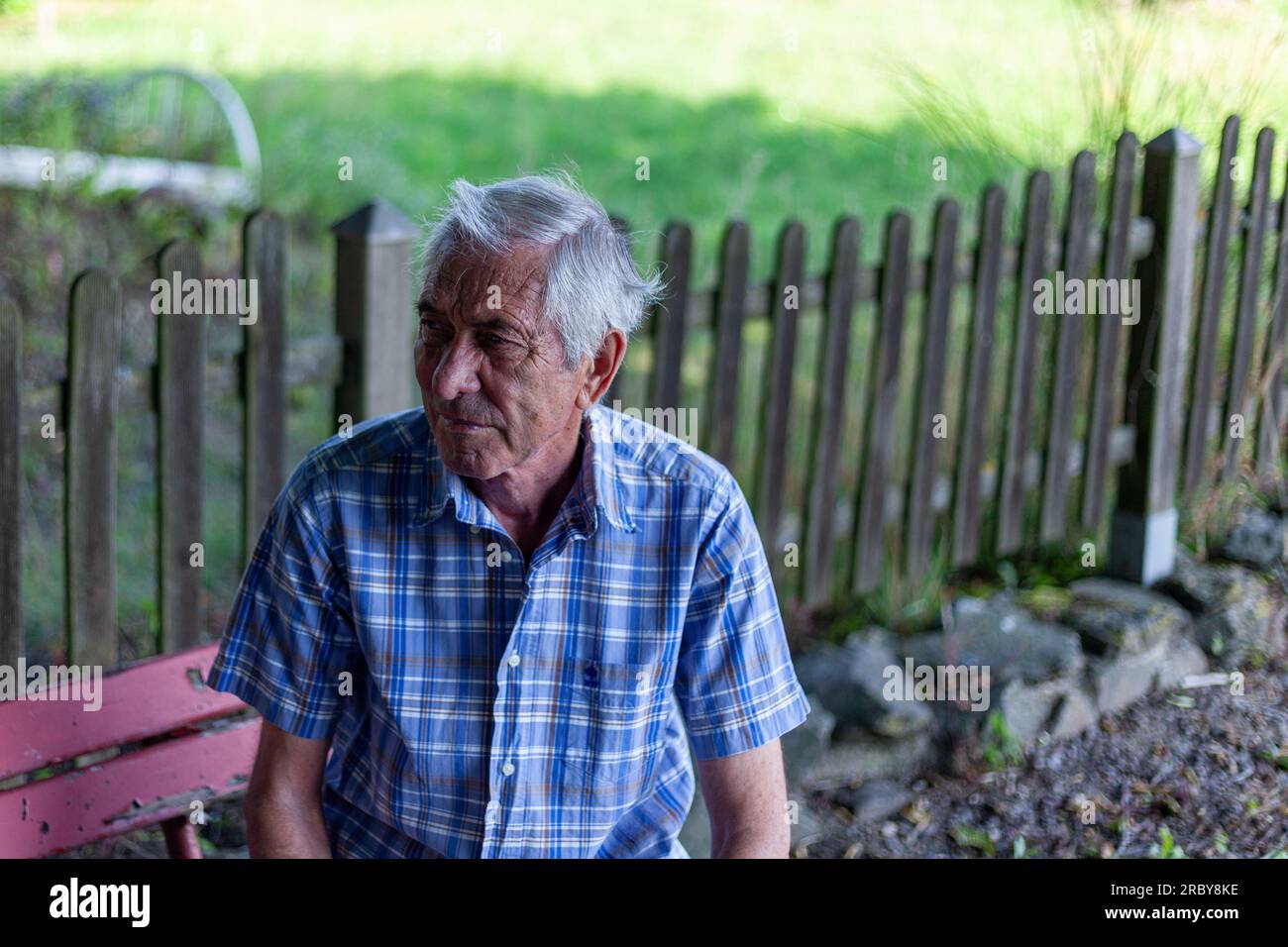 Homme âgé assis sur un banc dans le jardin et regardant la caméra Banque D'Images